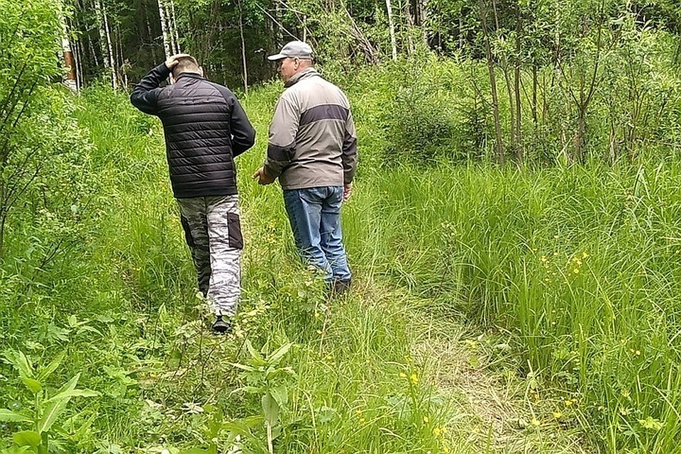 Сотрудник полиции и волонтер ищут потерявшегося рыбака в лесу.