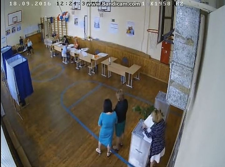 На записи видно, что пока одна женщина засовывает листы в урну, две других прикрывают ее махинации своими спинами. Фото: youtube.com